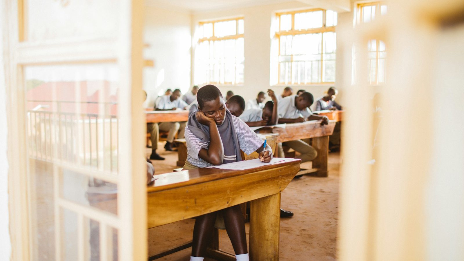 Secondary school students sitting an examination at wooden desks in a Ugandan classroom