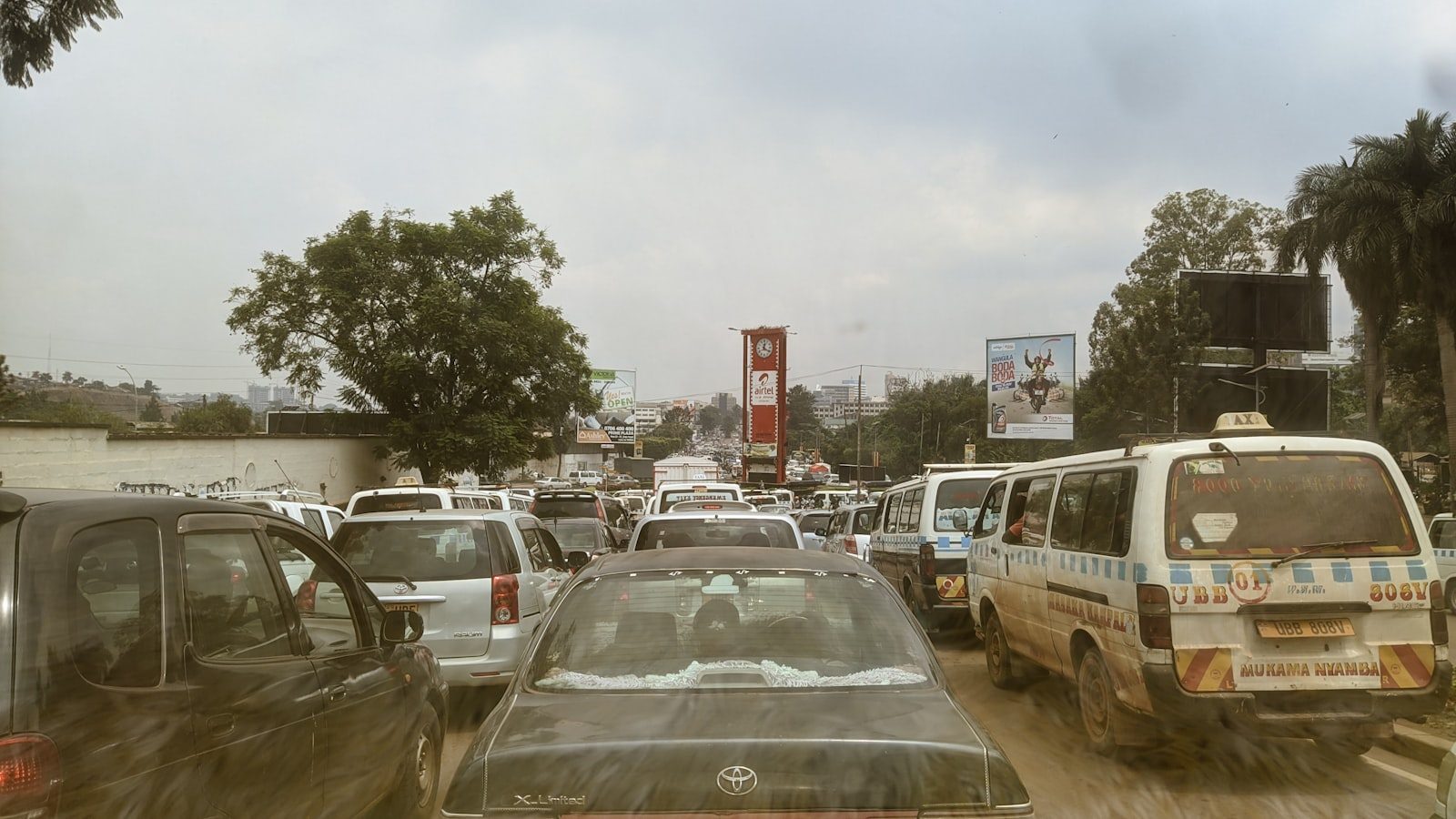 A Kampala street in heavy traffic, with telecom advertising hoardings above the road